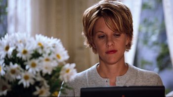 Movie still from “You've Got Mail” (1998), directed by Nora Ephron – A person using a computer near a flower; Medium shot, Over the shoulder angle