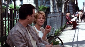 Movie still from “You've Got Mail” (1998), directed by Nora Ephron – A man and a woman sitting next to each other holding an apple; Medium shot, Over the shoulder angle