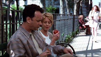 Movie still from “You've Got Mail” (1998), directed by Nora Ephron – A man and a woman sitting on a bench eating a tomato; Medium shot, Over the shoulder angle
