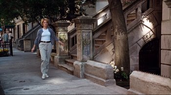 Movie still from “You've Got Mail” (1998), directed by Nora Ephron – A woman walking down a sidewalk next to a set of stairs; Wide shot, Low angle