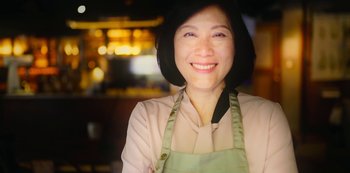 Movie still from “Archive 81” (2022), created by Rebecca Sonnenshine – A woman wearing an apron smiling for the camera; Close Up shot, Low angle
