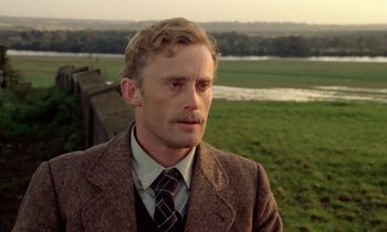A man wearing a suit and tie standing in front of a field