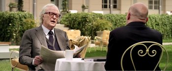 Movie still from “Youth” (2015), directed by Paolo Sorrentino – A man and a woman sitting at a table with a newspaper; Medium shot, Over the shoulder angle