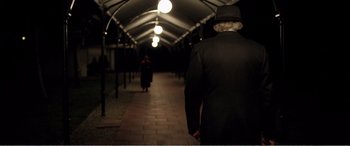 Movie still from “Youth” (2015), directed by Paolo Sorrentino – A man in a suit and hat walking down a walkway; Medium shot, Over the shoulder angle