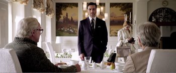 Movie still from “Youth” (2015), directed by Paolo Sorrentino – A man in a suit standing in front of a dining table; Medium shot, Over the shoulder angle