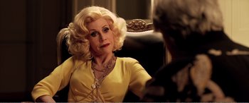 An older woman in a yellow dress sitting in a chair