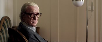 Movie still from “Youth” (2015), directed by Paolo Sorrentino – An older man wearing glasses sitting in front of a wall; Close Up shot, Over the shoulder angle