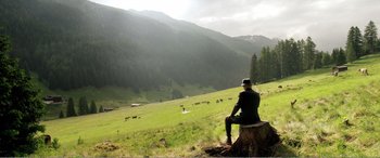 Movie still from “Youth” (2015), directed by Paolo Sorrentino – A man sitting on top of a tree stump in the middle of a field; Wide shot, High angle