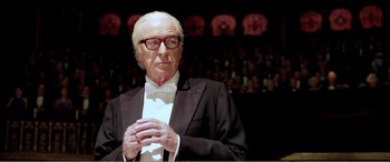 An older man in a tuxedo is holding his hands together