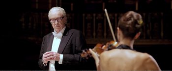 Movie still from “Youth” (2015), directed by Paolo Sorrentino – An older man in a tuxedo is playing the violin; Medium shot, Over the shoulder angle