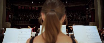 Movie still from “Youth” (2015), directed by Paolo Sorrentino – A woman with a ponytail is looking at a orchestra; Medium shot, Low angle