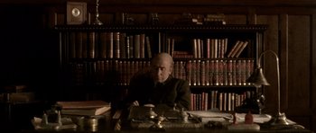 Movie still from “Youth Without Youth” (2007), directed by Francis Ford Coppola – An older man sitting at a desk in front of a bookshelf; Medium shot, High angle