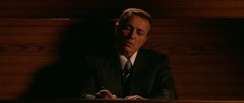 Movie still from “Youth Without Youth” (2007), directed by Francis Ford Coppola – A man in a suit and tie sitting at a table; Medium shot, High angle