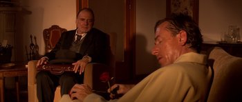 Movie still from “Youth Without Youth” (2007), directed by Francis Ford Coppola – A man sitting in front of another man holding a red rose; Medium shot, Over the shoulder angle