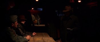 Movie still from “Youth Without Youth” (2007), directed by Francis Ford Coppola – A man wearing a hat sitting at a wooden table; Medium shot, Over the shoulder angle