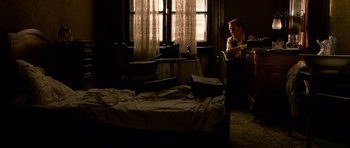 Movie still from “Youth Without Youth” (2007), directed by Francis Ford Coppola – A man sitting in a chair next to a bed in front of a window; Wide shot, High angle