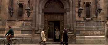 Movie still from “Youth Without Youth” (2007), directed by Francis Ford Coppola – A group of people walking in front of an entrance to a building; Wide shot, Low angle