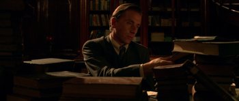 Movie still from “Youth Without Youth” (2007), directed by Francis Ford Coppola – A man sitting at a desk in front of a stack of books; Medium shot, High angle