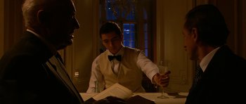 Movie still from “Youth Without Youth” (2007), directed by Francis Ford Coppola – A man in a white vest and bow tie holding a wine glass; Medium shot, Low angle