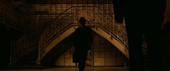 Movie still from “Youth Without Youth” (2007), directed by Francis Ford Coppola – A man in a suit and hat walking down a staircase at night; Wide shot, Low angle