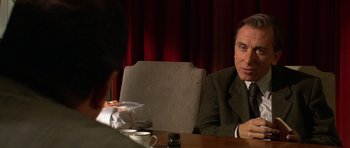 Movie still from “Youth Without Youth” (2007), directed by Francis Ford Coppola – A man sitting at a table with a bag in front of him; Close Up shot, Over the shoulder angle