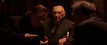 Movie still from “Youth Without Youth” (2007), directed by Francis Ford Coppola – A group of people sitting around a table with a candle; Medium shot, Over the shoulder angle