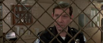 Movie still from “Zabriskie Point” (1970), directed by Michelangelo Antonioni – A man in a police uniform behind a chain link fence; Close Up shot, Low angle