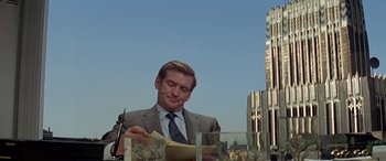 Movie still from “Zabriskie Point” (1970), directed by Michelangelo Antonioni – A man in a suit and tie writing on a piece of paper; Medium shot, Low angle