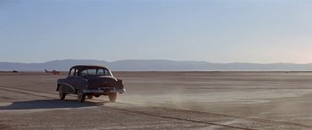 Movie still from “Zabriskie Point” (1970), directed by Michelangelo Antonioni – An old car driving down a road in the middle of the desert; Extreme Wide shot, Low angle