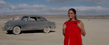 Movie still from “Zabriskie Point” (1970), directed by Michelangelo Antonioni – A woman standing in front of an old car in the desert; Medium shot, Low angle