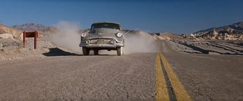 Movie still from “Zabriskie Point” (1970), directed by Michelangelo Antonioni – An old car driving down a road near a hill; Wide shot, Low angle