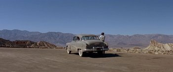 Movie still from “Zabriskie Point” (1970), directed by Michelangelo Antonioni – A man standing next to an old car on the side of a dirt road; Extreme Wide shot, Low angle