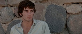 Movie still from “Zabriskie Point” (1970), directed by Michelangelo Antonioni – A man sitting on the ground in front of a stone wall; Close Up shot, Over the shoulder angle