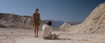 Movie still from “Zabriskie Point” (1970), directed by Michelangelo Antonioni – A man kneeling down next to a woman on a beach; Wide shot, Low angle