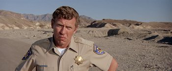 Movie still from “Zabriskie Point” (1970), directed by Michelangelo Antonioni – A man in a uniform standing in the middle of the desert; Close Up shot, Low angle