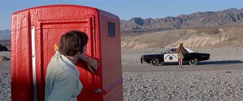 Movie still from “Zabriskie Point” (1970), directed by Michelangelo Antonioni – A man standing in front of a red door and a police car; Wide shot, Low angle