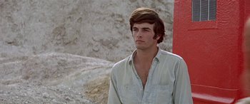 Movie still from “Zabriskie Point” (1970), directed by Michelangelo Antonioni – A man with long brown hair wearing a white shirt; Close Up shot, Low angle