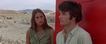 Movie still from “Zabriskie Point” (1970), directed by Michelangelo Antonioni – A man and a woman standing next to each other in front of a red wall; Medium shot, Low angle