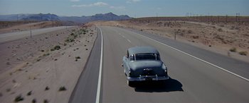Movie still from “Zabriskie Point” (1970), directed by Michelangelo Antonioni – An old car driving down a road in the middle of the desert; Extreme Wide shot, High angle
