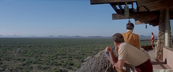 Movie still from “Zabriskie Point” (1970), directed by Michelangelo Antonioni – A man sitting on top of a rock looking out over a desert landscape; Wide shot, Over the shoulder angle