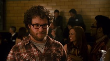 Movie still from “Zack and Miri Make a Porno” (2008), directed by Kevin Smith – A man with a beard and glasses in front of a group of people; Medium shot, Over the shoulder angle