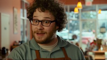 Movie still from “Zack and Miri Make a Porno” (2008), directed by Kevin Smith – A man wearing glasses and an apron is smiling; Close Up shot, Over the shoulder angle