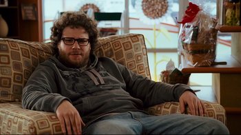 Movie still from “Zack and Miri Make a Porno” (2008), directed by Kevin Smith – A man sitting in a chair wearing glasses; Medium shot, Over the shoulder angle