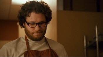 Movie still from “Zack and Miri Make a Porno” (2008), directed by Kevin Smith – A man wearing an apron and glasses looking to his left; Close Up shot, Over the shoulder angle