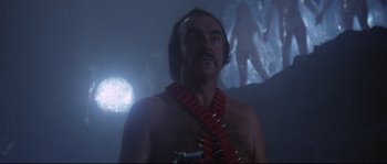 Movie still from “Zardoz” (1974), directed by John Boorman – A man with a bunch of bullet casings around his neck; Medium shot, Low angle