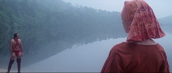Movie still from “Zardoz” (1974), directed by John Boorman – A man in a red jacket standing in front of a body of water; Close Up shot, High angle