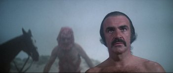 Movie still from “Zardoz” (1974), directed by John Boorman – A man with a beard and mustache is looking into the distance; Close Up shot, Over the shoulder angle