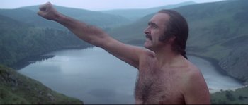 Movie still from “Zardoz” (1974), directed by John Boorman – A man with a beard is standing on a cliff; Medium shot, Low angle