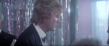 Movie still from “Zardoz” (1974), directed by John Boorman – A man with long blonde hair wearing a suit and tie; Close Up shot, Over the shoulder angle