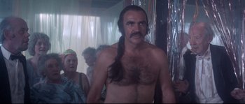 Movie still from “Zardoz” (1974), directed by John Boorman – A man with long hair is standing in front of a group of people; Medium shot, Over the shoulder angle